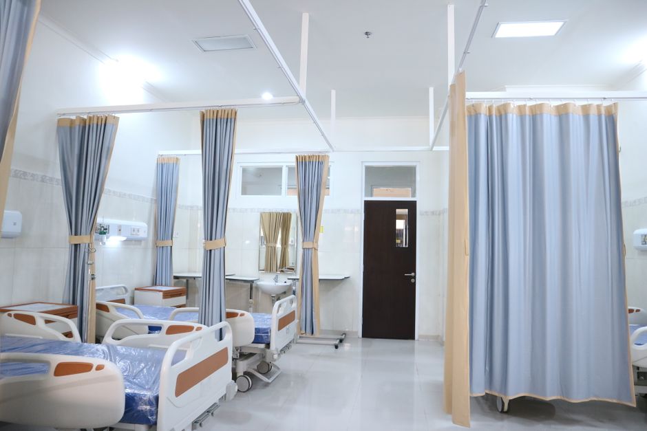 Clean and modern hospital ward with beds and privacy curtains in Surabaya, Indonesia.