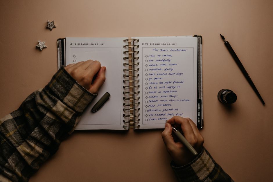 Overhead shot of a person writing New Year's resolutions in a notebook on a desk.