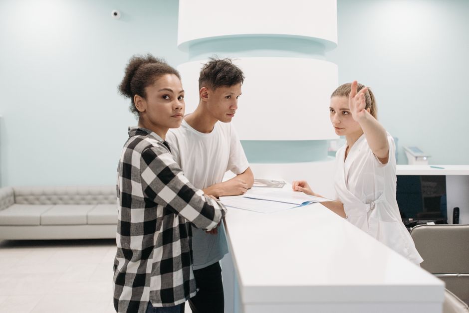 Two patients at hospital reception desk interacting with receptionist in white attire.
