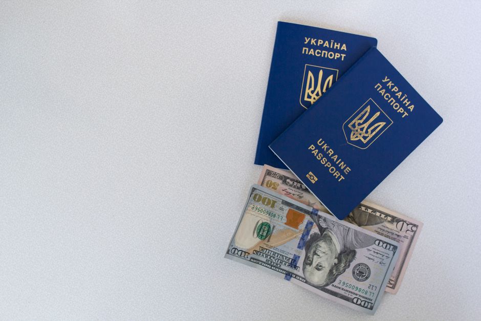 Top view of two Ukrainian passports with US dollar bills on a white surface.