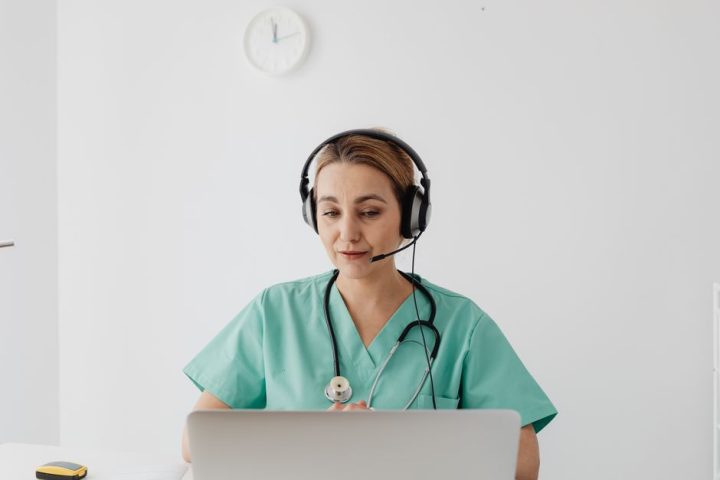 A female doctor in scrubs using a laptop for a virtual consultation, enhancing telemedicine.